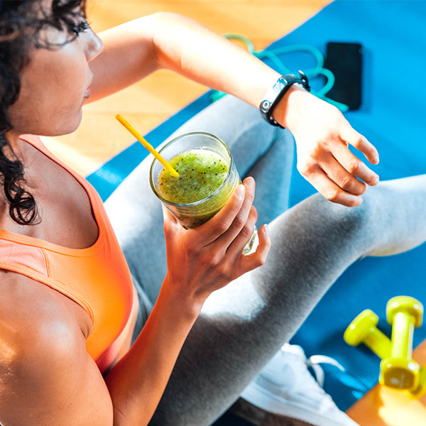 Sporty woman in sportswear training at home drinking fresh smoothie